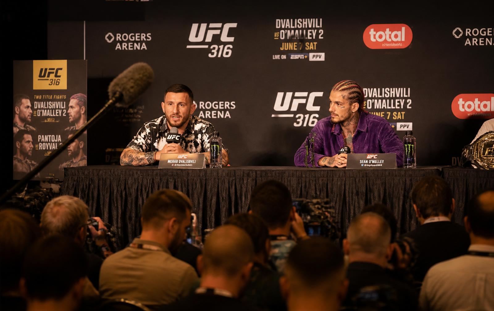 UFC main-event press conference in Vancouver with fighters seated behind a branded backdrop and press in the foreground.