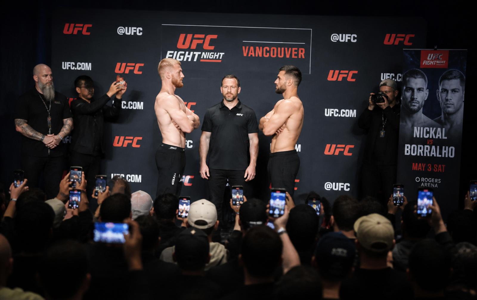 Two UFC fighters facing off at the ceremonial weigh-in stage in Vancouver with a crowd filming on phones.