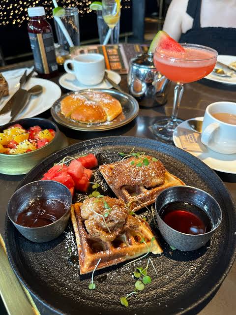 Chicken and waffles brunch plate with dipping sauces, watermelon, mimosa and coffee on a dark table.