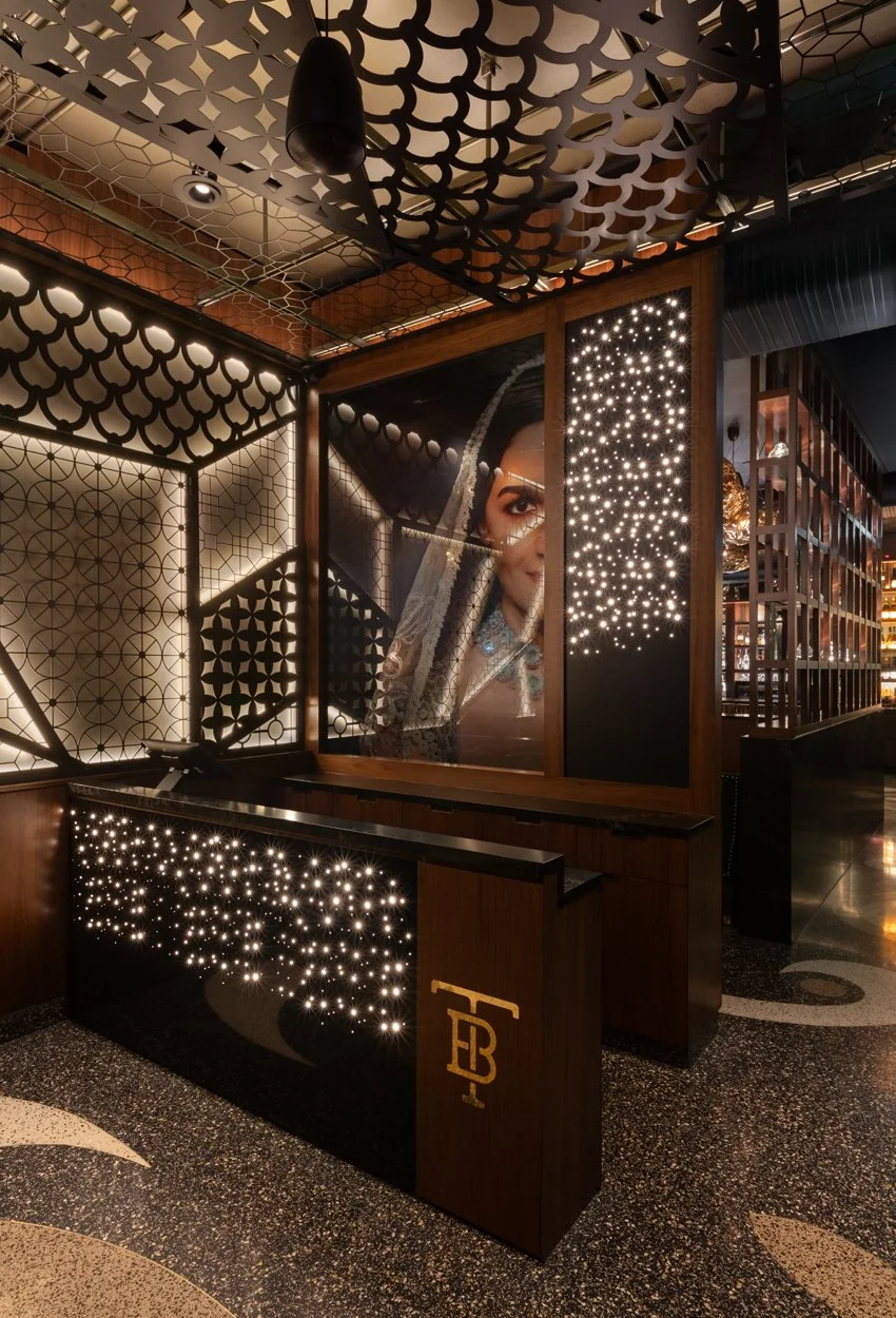 Interior host stand with laser-cut screens, terrazzo floor, gold TB monogram and a large portrait of a bride behind a starlight veil.