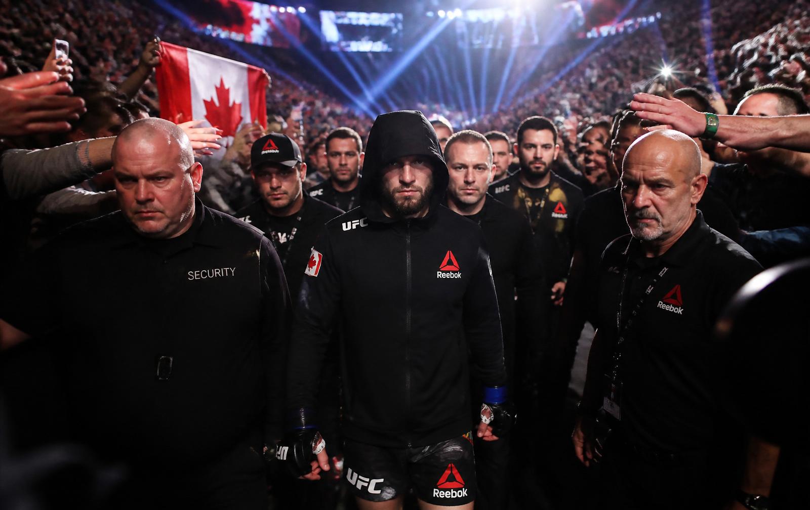 UFC fighter walking out through a corridor of security and cornermen with a Canadian flag raised in the crowd.