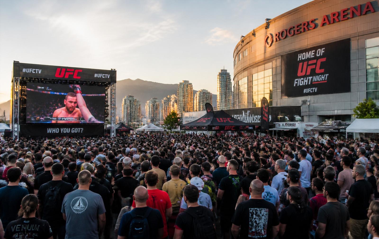 Large crowd gathered outside Rogers Arena Vancouver watching UFC content on a giant outdoor LED screen at golden hour.
