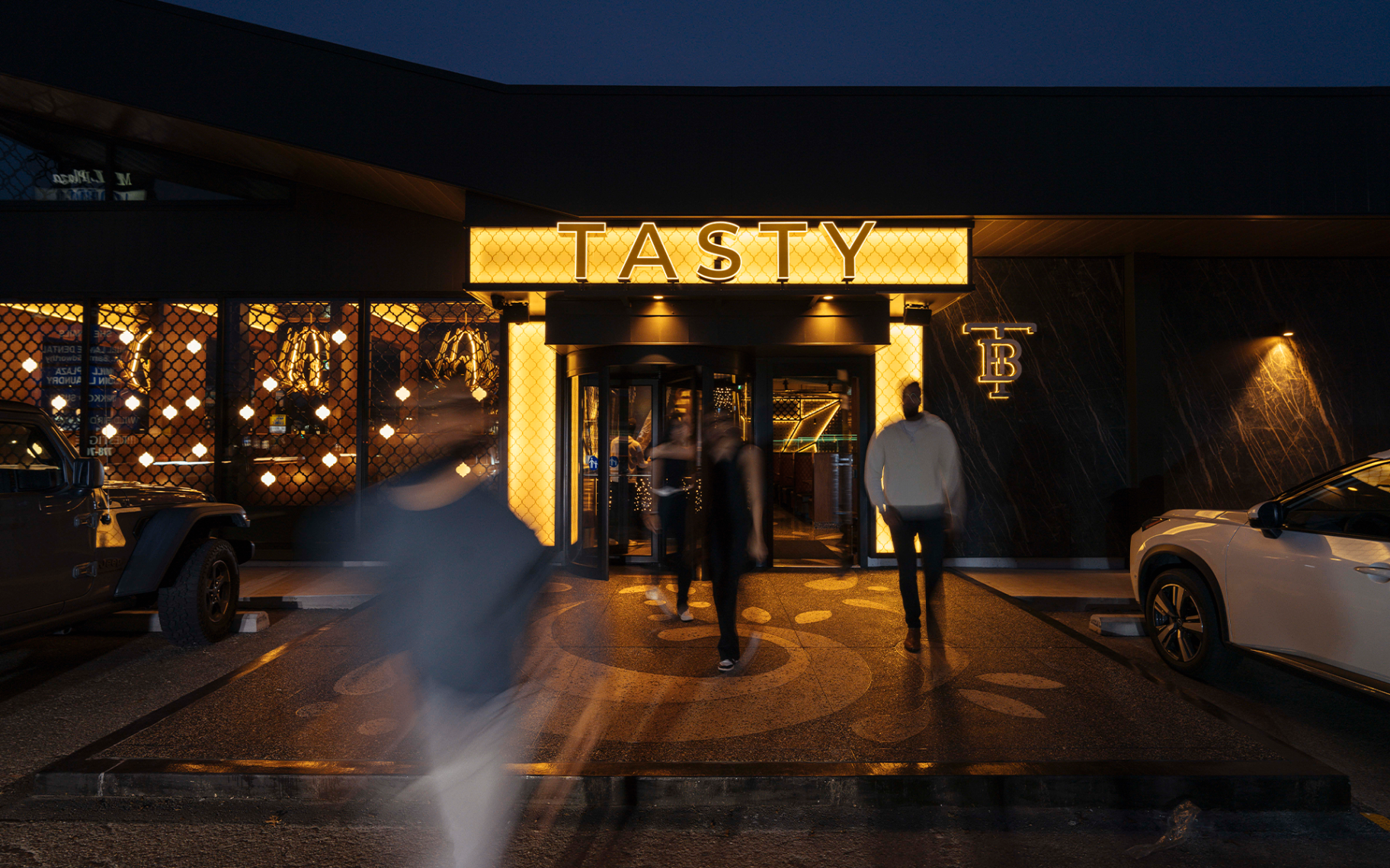 Illuminated TASTY marquee above the Abbotsford entrance at dusk with guests walking in through the revolving door.