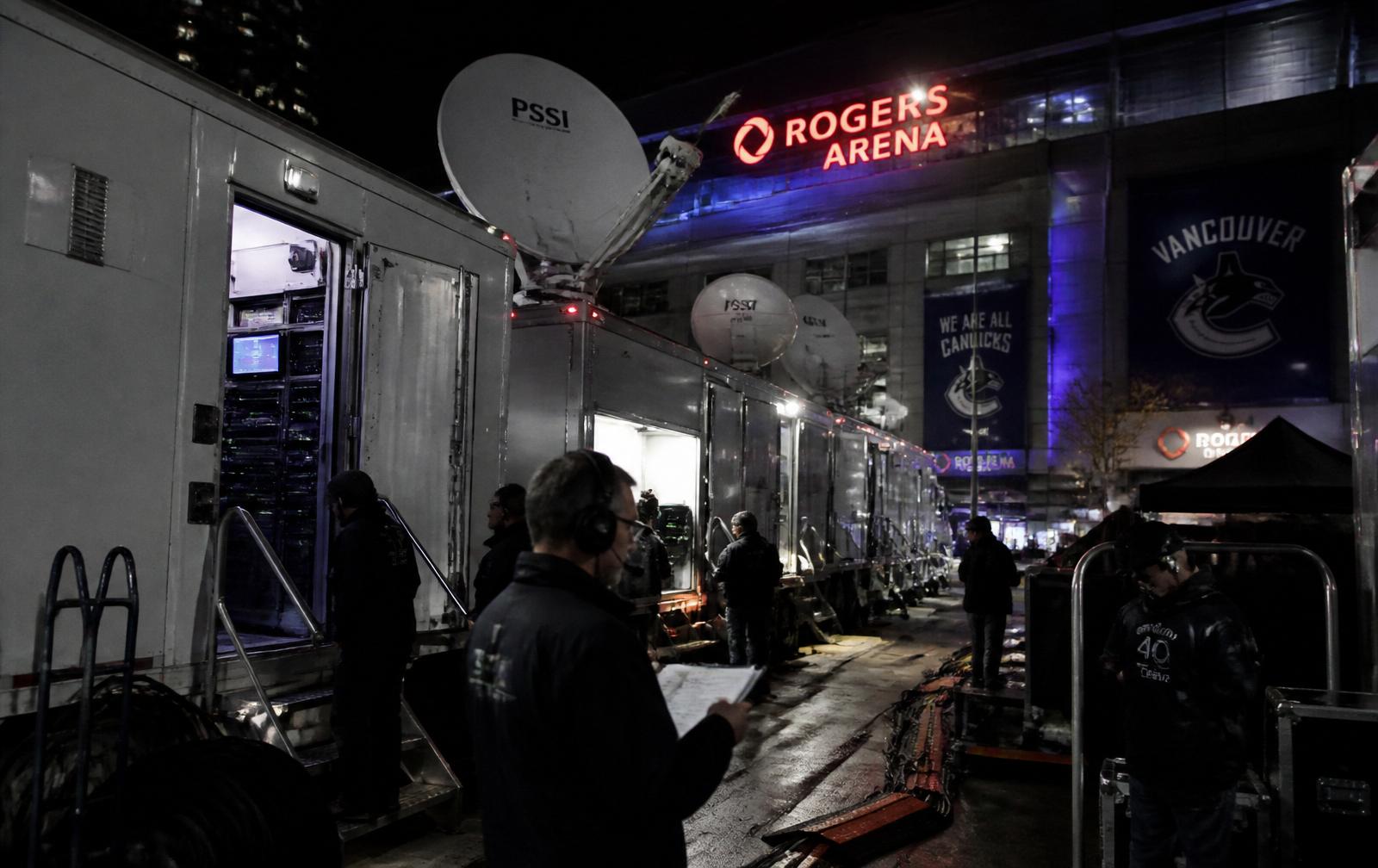 Broadcast trucks and satellite uplink dishes staged outside Rogers Arena at night for a UFC event.